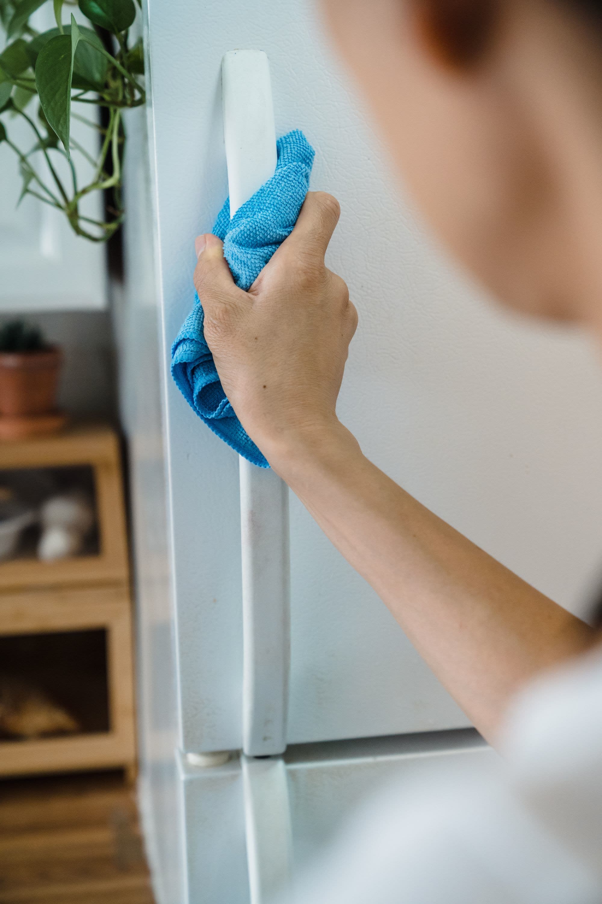 Hand torkar kylskåpshandtaget med en blå mikrofiberduk