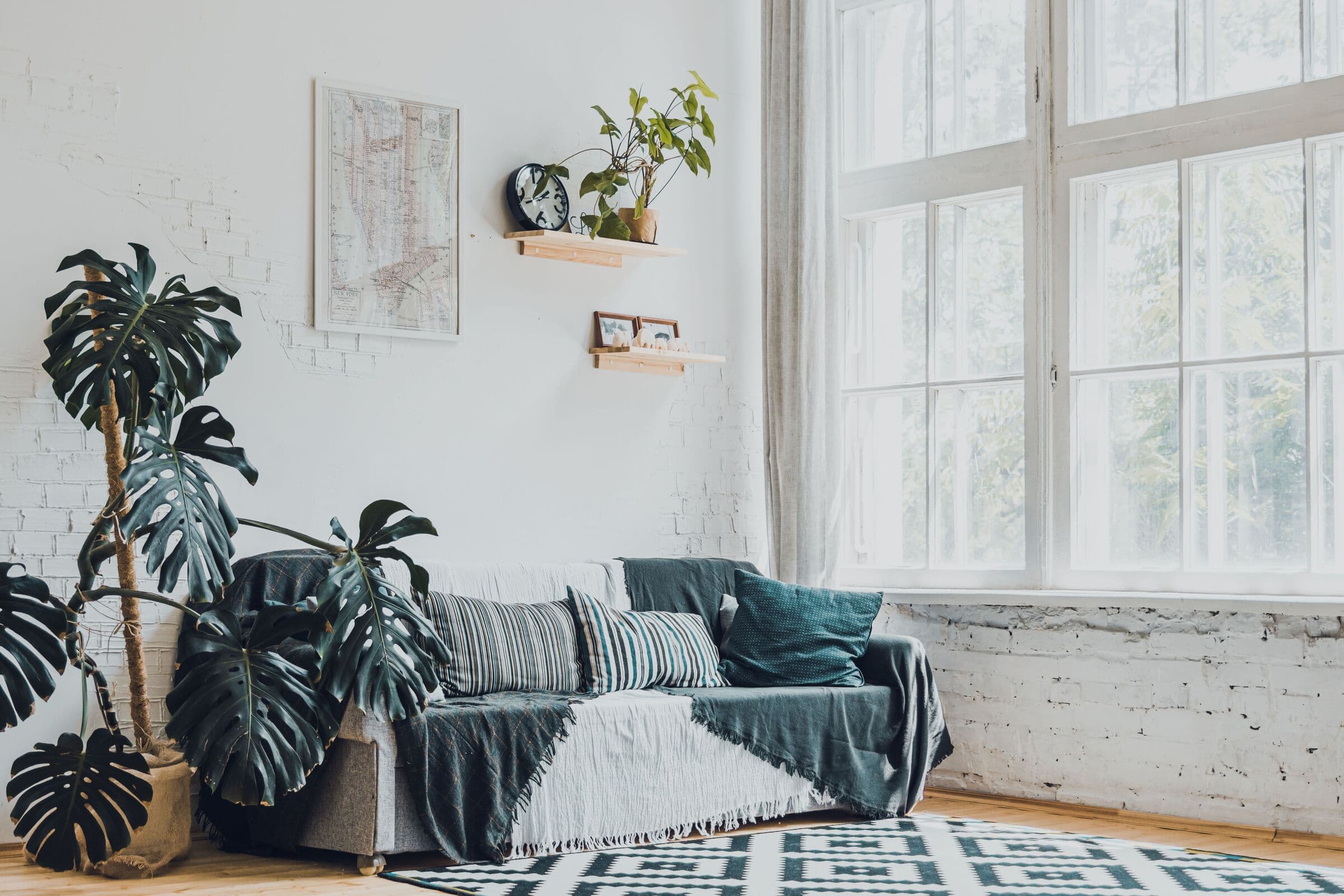 Ljust vardagsrum med soffa, monstera och stora spröjsade fönster